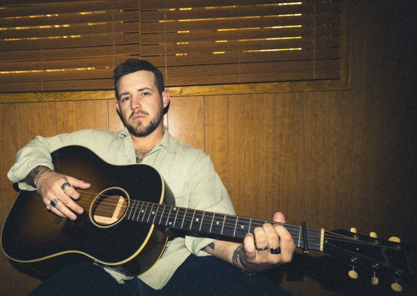 A man wearing a green shirt holding an acoustic guitarx